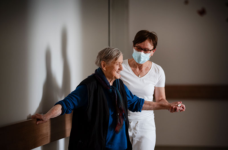 Medicinska sestra i starija žena koja se smiješi dok joj medicinska sesta pomaže hodati.